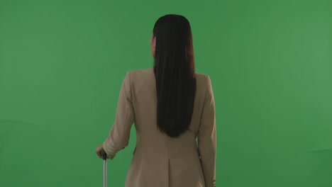 vista trasera mujer de negocios asiática viajera con equipaje de pie en el estudio de fondo de la pantalla verde, durante la hora de la puesta del sol