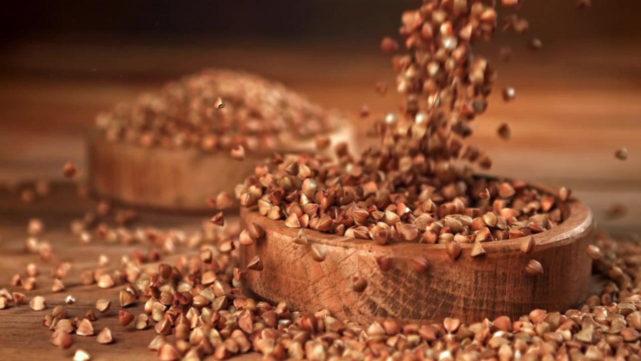 Buchweizenkörner fallen in Zeitlupe in eine Holzschale