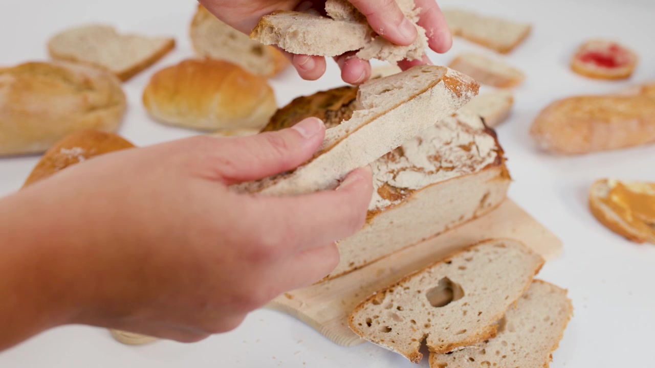 Primo piano di mani che spezzano pane artigianale a lievitazione naturale su un tagliere di legno con luce intensa.