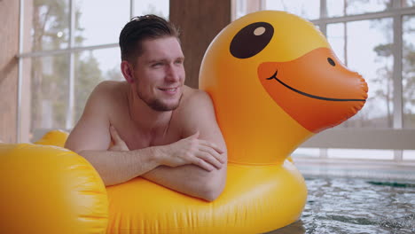 cheerful-man-is-enjoying-and-relaxing-in-spa-center-with-thermal-pool-lying-on-funny-inflatable-circle