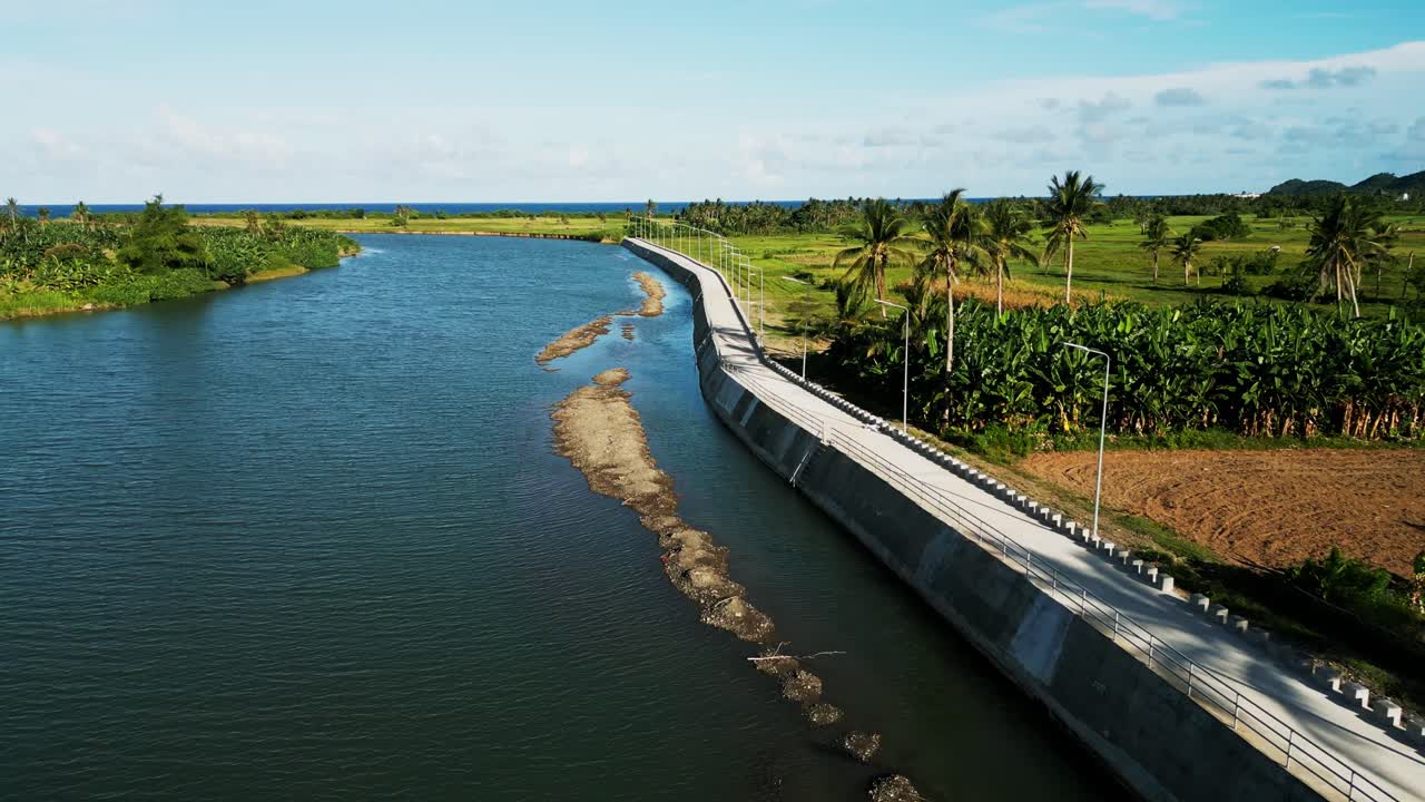 Aerial drone shot of river dike and boulevard next to lush tropical island scenery and quaint river embankment at Pajo, Catanduanes, Philippines