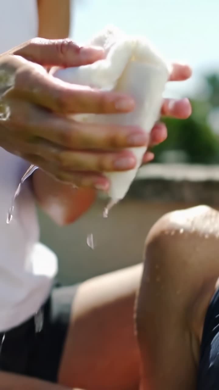 Video verticale: Strizzando un panno in un secchio grigio a bordo piscina, mani che rinfrescano una donna in costume da bagno, spazio per il testo.