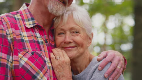 un primer plano de una pareja de ancianos jubilados que se abrazan caminando juntos por el bosque.