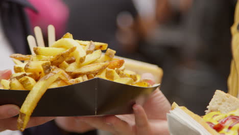 Close-Up-Of-Two-Women-Buying-Hot-Dogs-And-Fries-From-Street-Food-Market-Stall