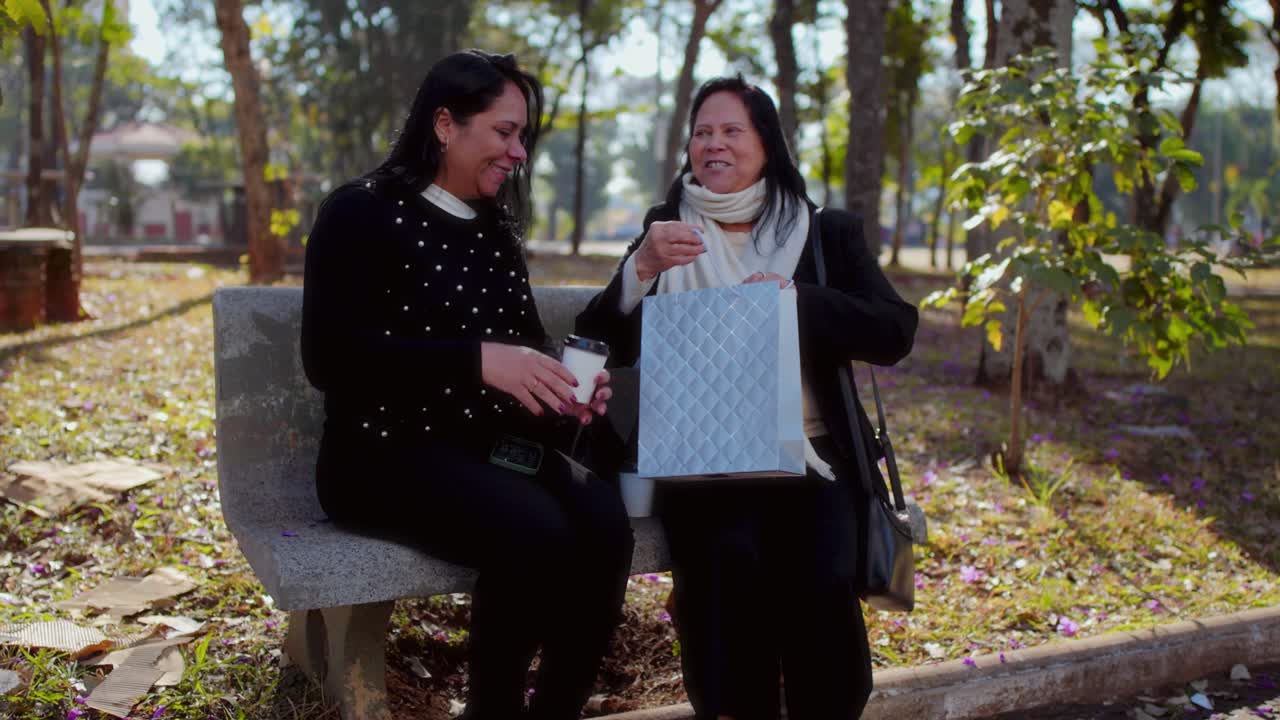 Two Women Share a Joyful Moment with a Gift Bag on a Park Bench