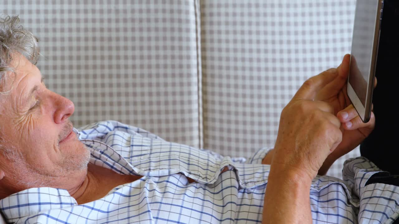 hombre mayor con tableta digital acostado en el sofá en el porche 4k
