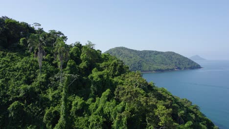 Flying-over-mountains-and-jungle-revealing-a-large-island-on-the-green-coast,-Costa-Verde-of-sunny-Brazil---Aerial-view