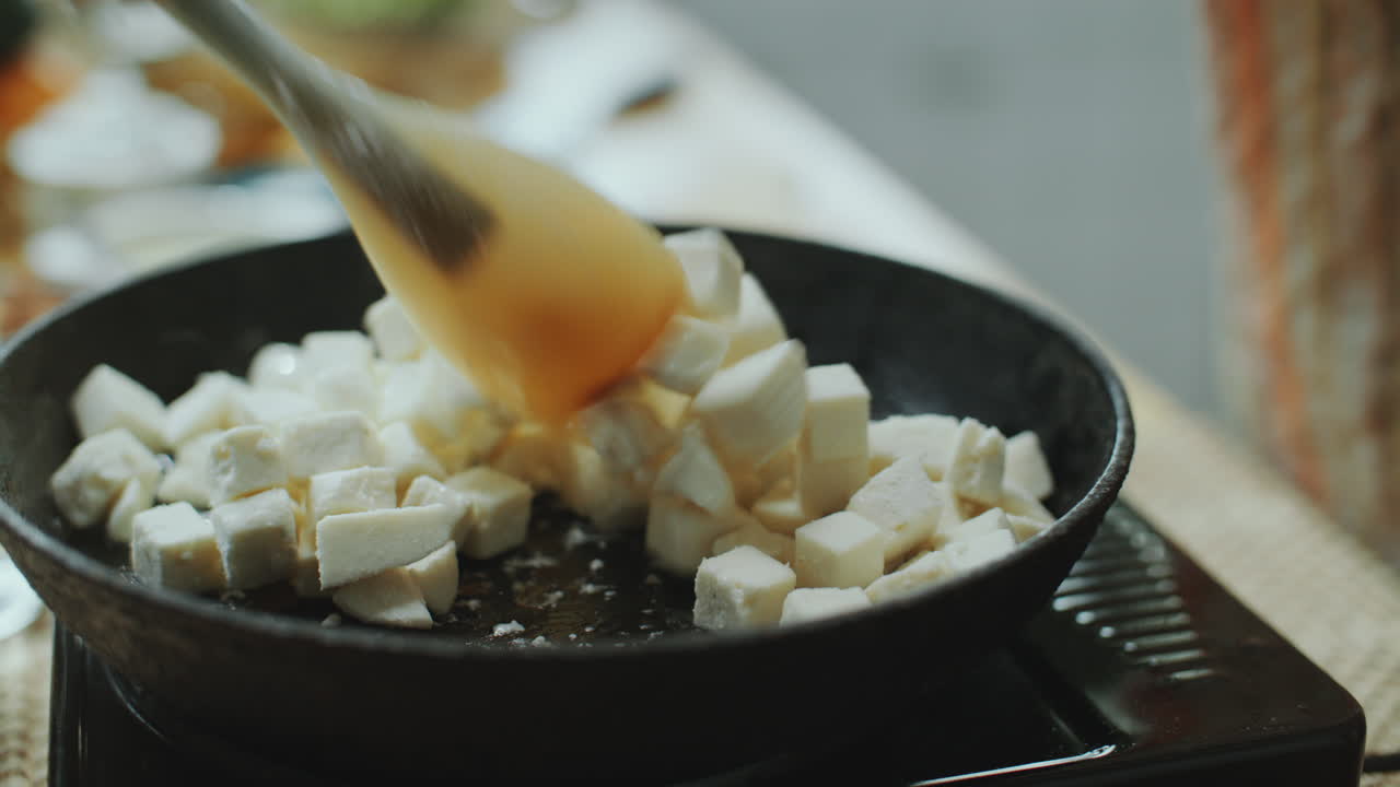 agitar cubos de paneer fresco con una espátula en una sartén caliente
