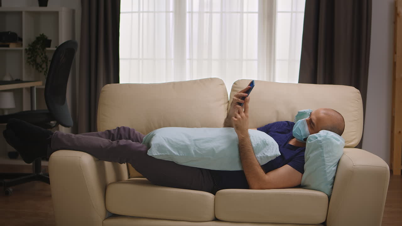 hombre aburrido con máscara de protección acostado en el sofá