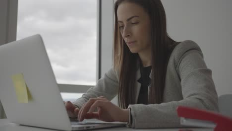 Close-up-of-young-satisfied-businesswoman-working-on-laptop-in-corporate-office