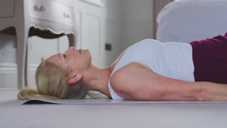 Active-Mature-Woman-Exercising-Doing-Yoga-On-Mat-At-Home