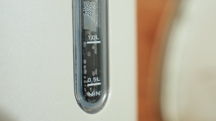 Close up of electric kettle water level indicator showing bubbles and steam rising inside during boiling process, highlighting transparent gauge markings in bright kitchen