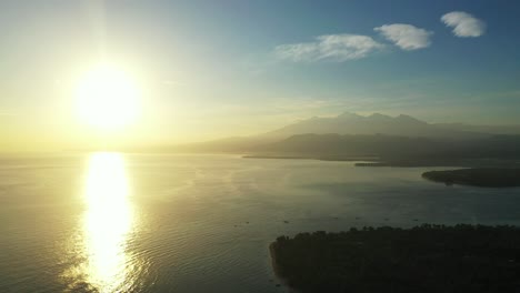 sunset over ocean horizon, glowing yellow sky reflecting on calm sea surface washing shore of tropical islands, bali