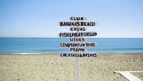 a sign at a tropical sandy beach showing directions for different places for food and drinks