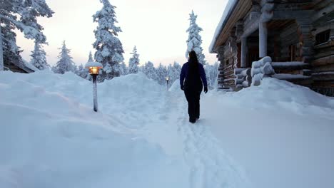 chica camina junto a la cabaña en el país de las maravillas de invierno nevado en laplandia, finlandia, círculo ártico