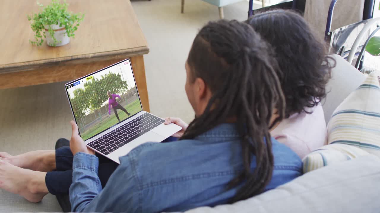 Casal birracial usando notebook com um jogador de futebol masculino afro-americano jogando uma partida na tela