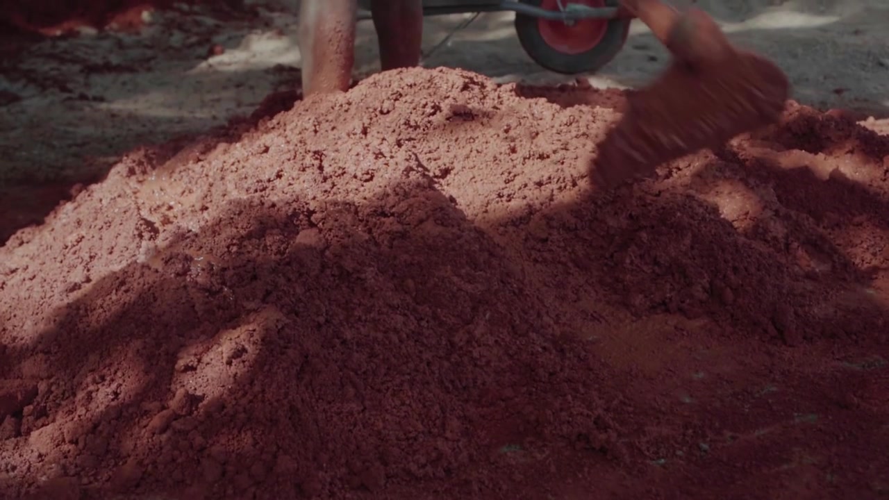 Brazilian worker mixing red clay and sand with a hoe. Traditional building technique for sustainable housing, also known as wattle and daub