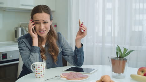 mujer seria teniendo una llamada telefónica desagradable sentada en la cocina.