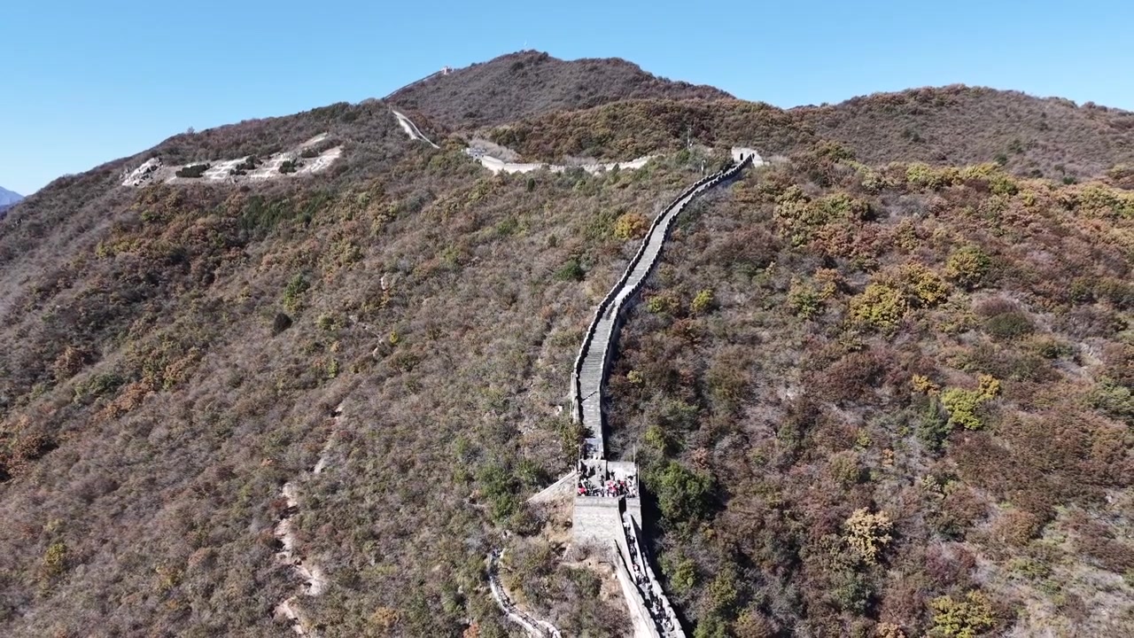 Vista aérea estática aproximada da Grande Muralha atravessando um cume de montanha árido em direção a um pico distante, com arbustos de outono cobrindo as encostas em ambos os lados, Distrito de Huairou, Pequim, China