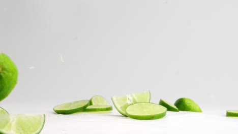 slices and wedges of bright green limes bouncing on white table top in slow motion