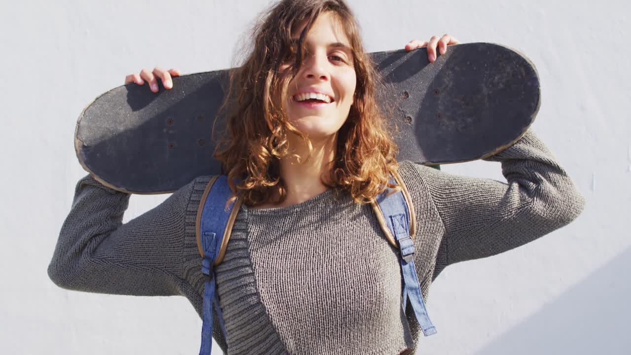 retrato de una mujer de raza mixta feliz con una patineta detrás de la cabeza sonriendo al sol
