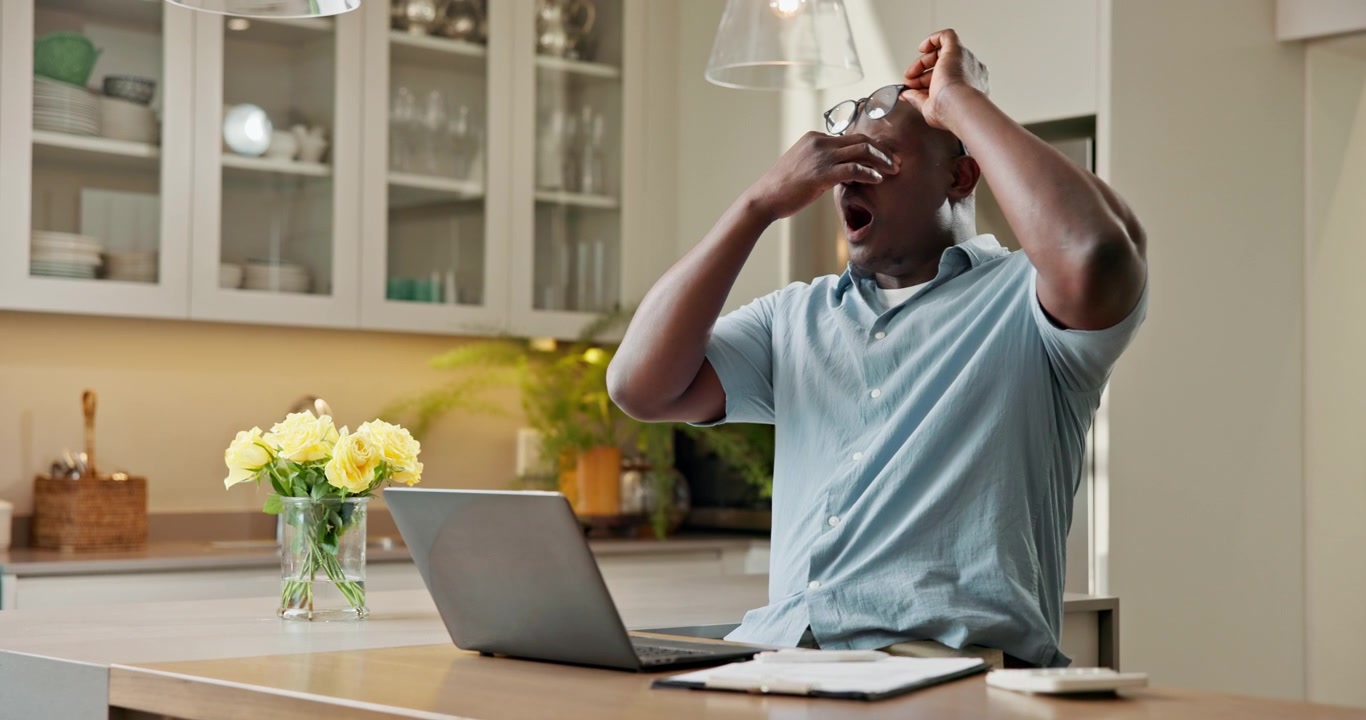 Tired Man Taking Off Glasses and Yawning While Working on Laptop