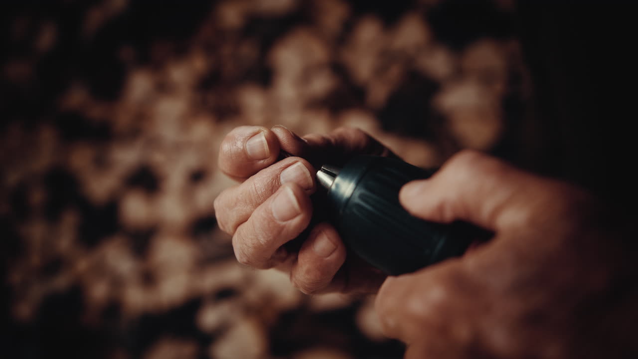 A slow motion of the carpenter fixing the bit of the drill on the blurry background