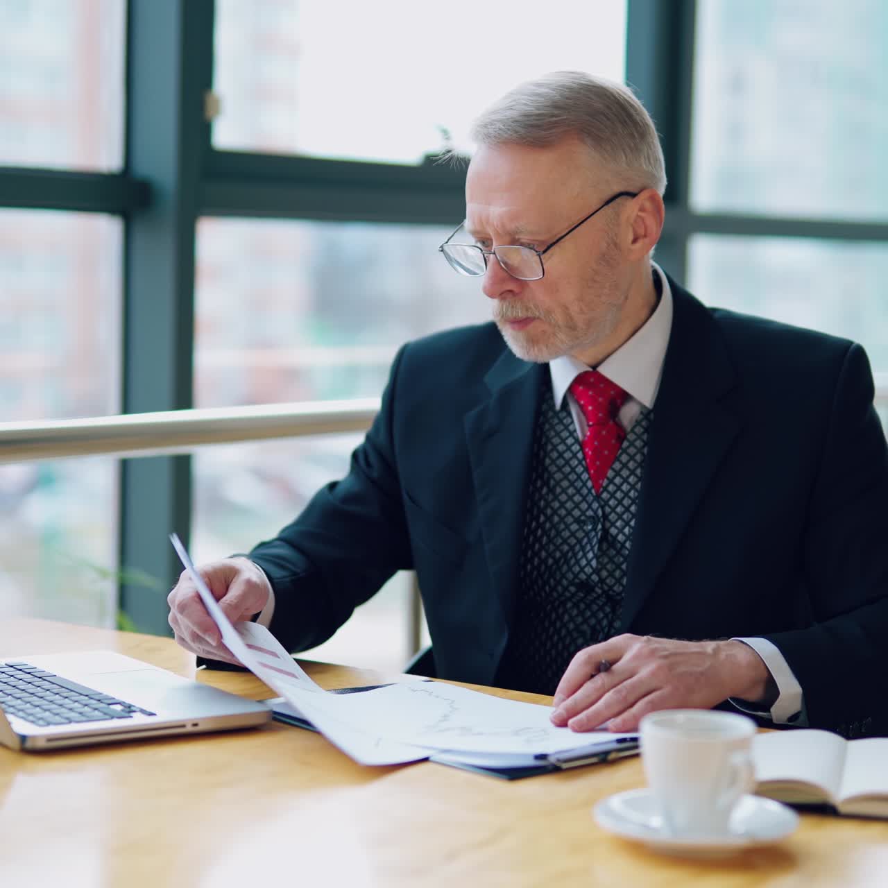 Smart mature businessman working in the office. Senior man in elegant suit sitting at the desk and using notebook in his work. Business concept.