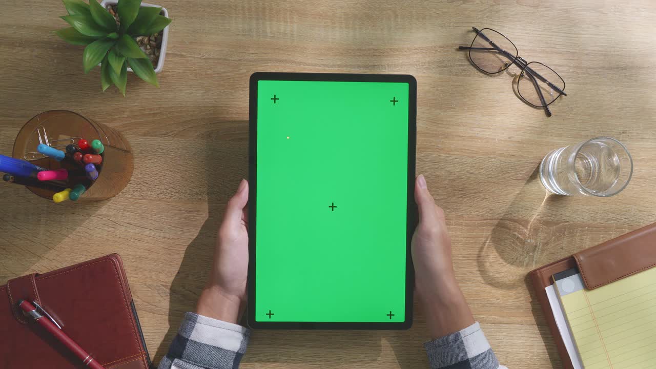 persona sosteniendo una tableta con una pantalla verde en un escritorio de madera