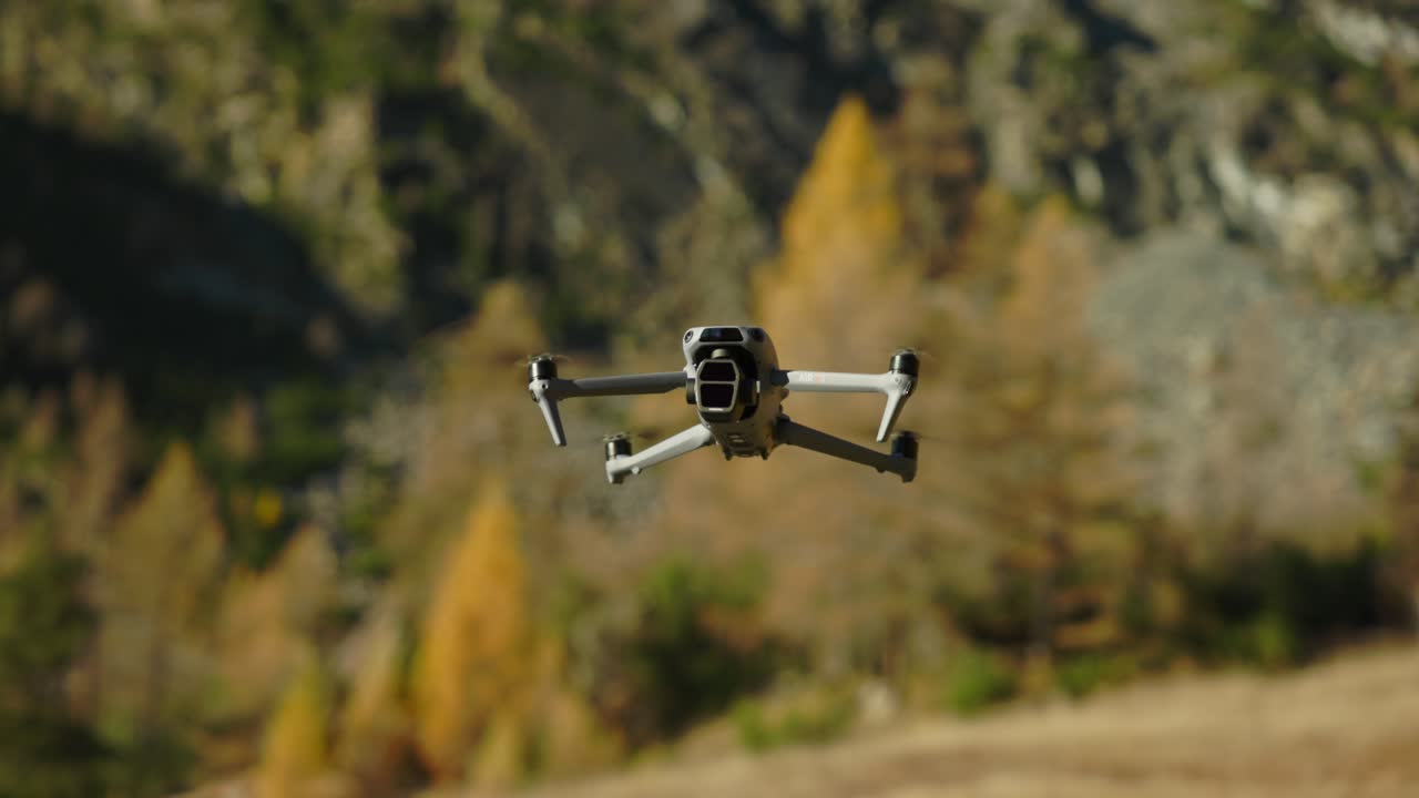 A quadcopter drone flying in a forested mountain background during sunny autumn.