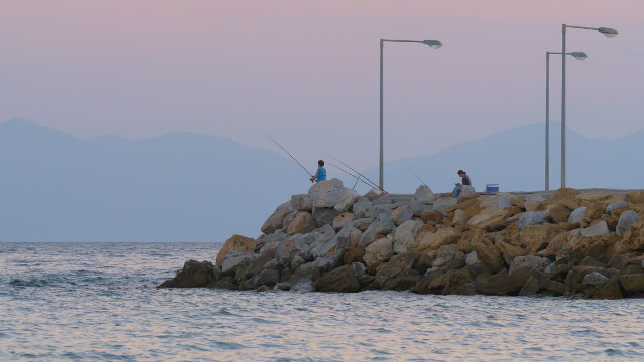 Man fishing in the sea from rocky pier evening scene