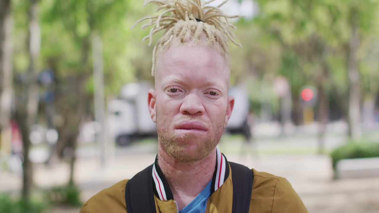 Portrait of albino african american man with dreadlocks in park looking at camera