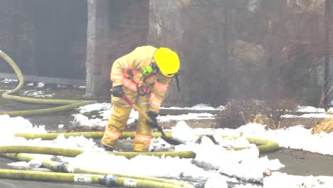 a firefighter shovels snow next to a fire hose, fire duty on public street, static