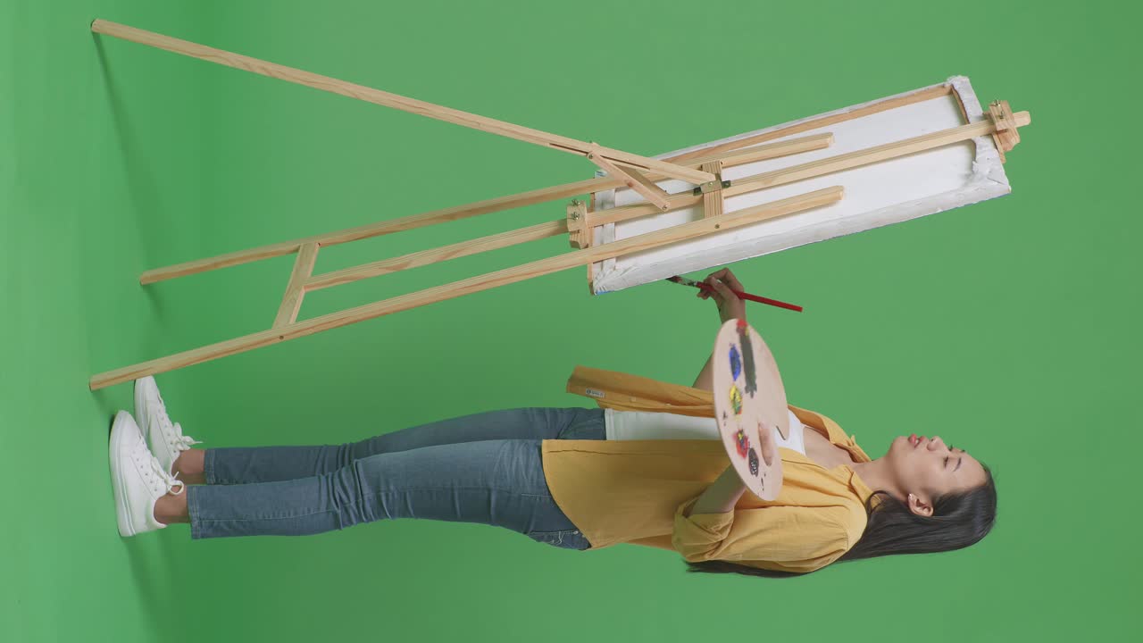 초록색 스크린 에 페인트 브러시 와 팔레트 를 들고 포즈 를 취 하는 여자 예술가