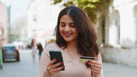 mujer india usando tarjeta de crédito teléfono inteligente mientras transfiere dinero compras compras en línea