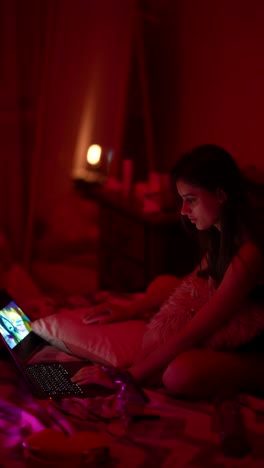 woman watching laptop in a red-lit bedroom at night