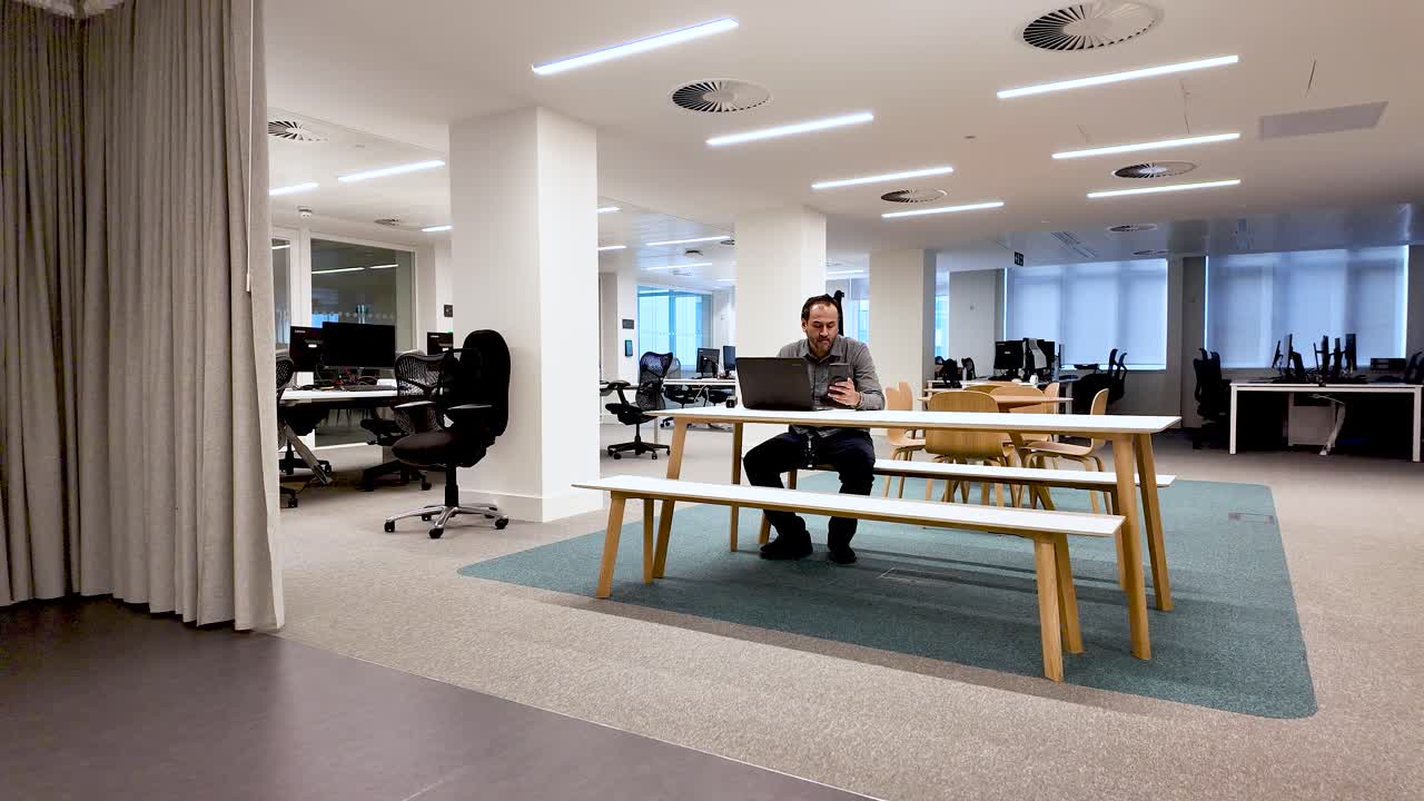 Hybrid Work And Flexible Office Space Lone South Asian Male Working At Table With Laptop And Phone