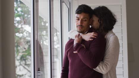 Romantic-hispanic-couple-embracing-cuddling-standing-in-window