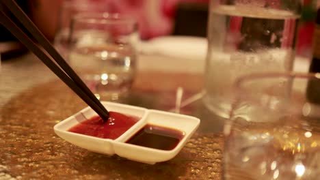 chopsticks dip into a dual sauce dish on a restaurant table, under warm ambient lighting
