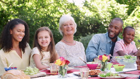 Familie-Und-Freunde-Essen-An-Einem-Tisch-Im-Garten-Zu-Mittag