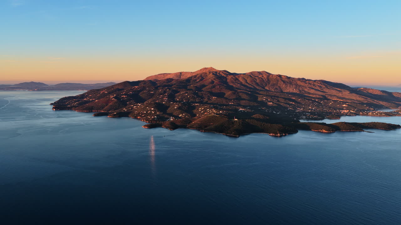 Aerial drone view of Corfu island near Ksamil, Albania showing rugged landscapes, green vegetation, and the island's coastline bathed in soft sunrise light