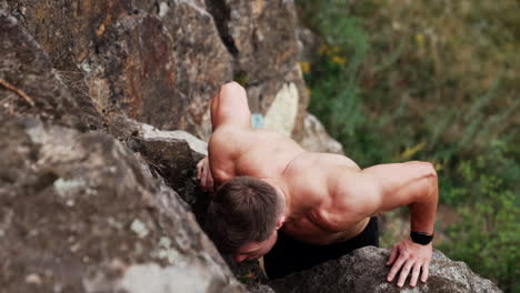 muscular caucasian man doing pushups among the rocks. sportsman using nature surrounding as a gym. workout in the nature. top view.