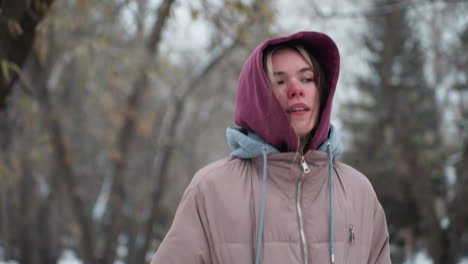 woman exercising in winter park with a thoughtful expression, dressed in warm hoodie and coat, she braves the cold weather, focusing on her workout against a blurred background