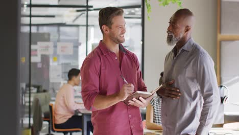 happy diverse business people holding notebook and discussing work at office