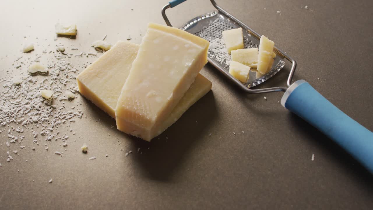Video of block of parmesan cheese and cheese grater cheese on wooden table