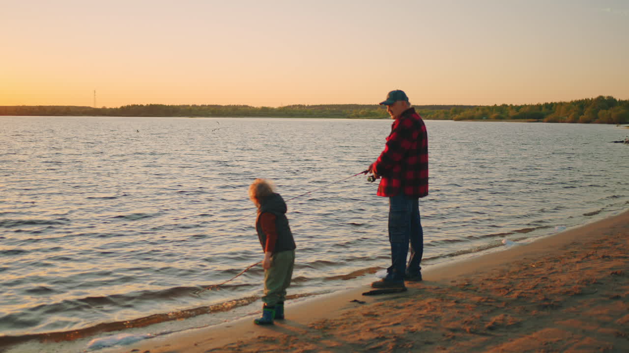 old fisher is catching faith in river by fishing-rod his little grandson is playing on sandy shore