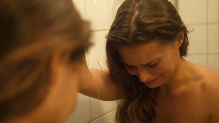 A woman with bruises and scars in her face from being punched and hit looks herself in the mirror