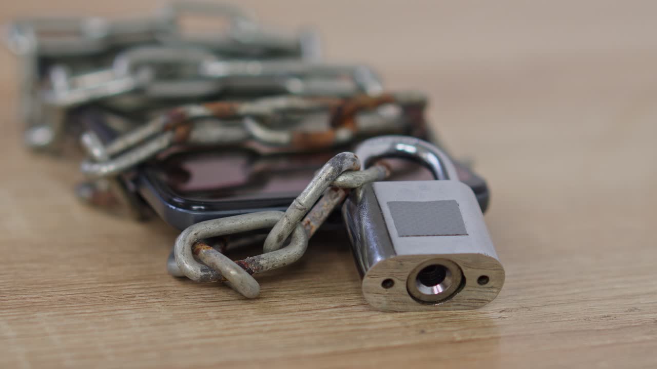 Smartphone wrapped in heavy iron chains on wooden desk for Cyber Security Concept