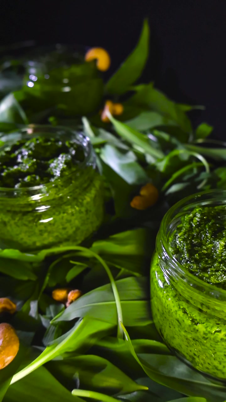 Koyu bir arka plan üzerinde taze yabani sarımsak yaprakları ve fındıklarla cam kavanozlarda ev yapımı vegan yabani sarımsak pestosu. Ayı sarımsağı olarak da bilinen allium ursinum'dan sağlıklı yeşil sos.