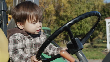 asian kid playing tractor driver, sitting behind the wheel of a tractor.